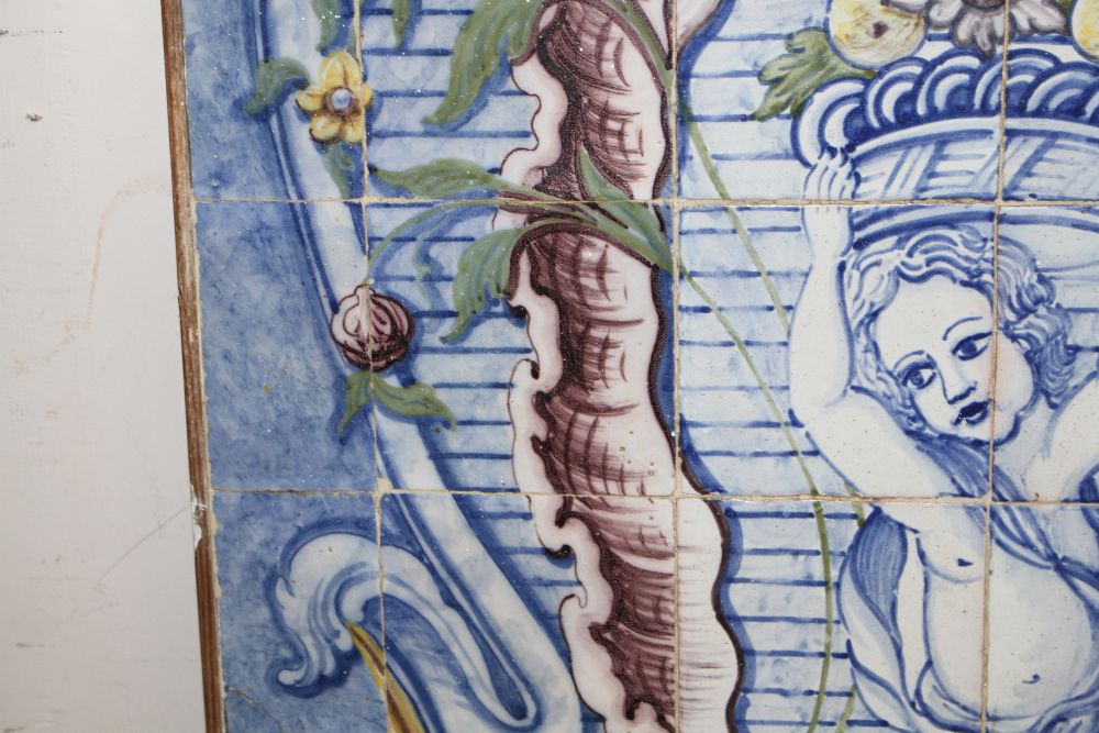 A Continental maiolica tile panel, depicting a putto holding aloft a basket of fruit, overall 90 x 72cm